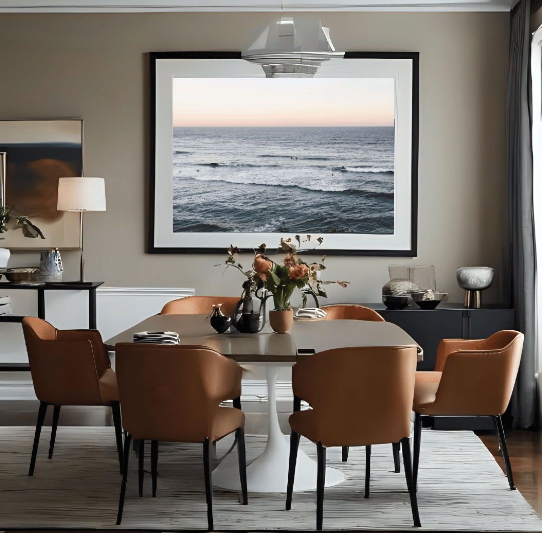 A large framed iconic Bondi beach photograph hangs on a beige wall above a dining table with six tan upholstered chairs in a modern dining room.