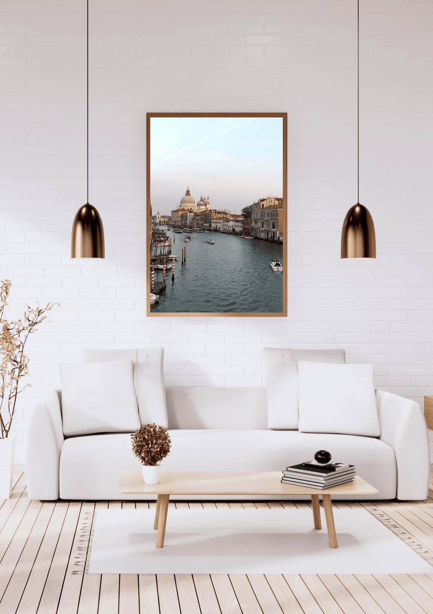 A framed art print depicting a scenic canal view of Venice, hung on a white brick wall above a modern white sofa in a bright, contemporary living room.