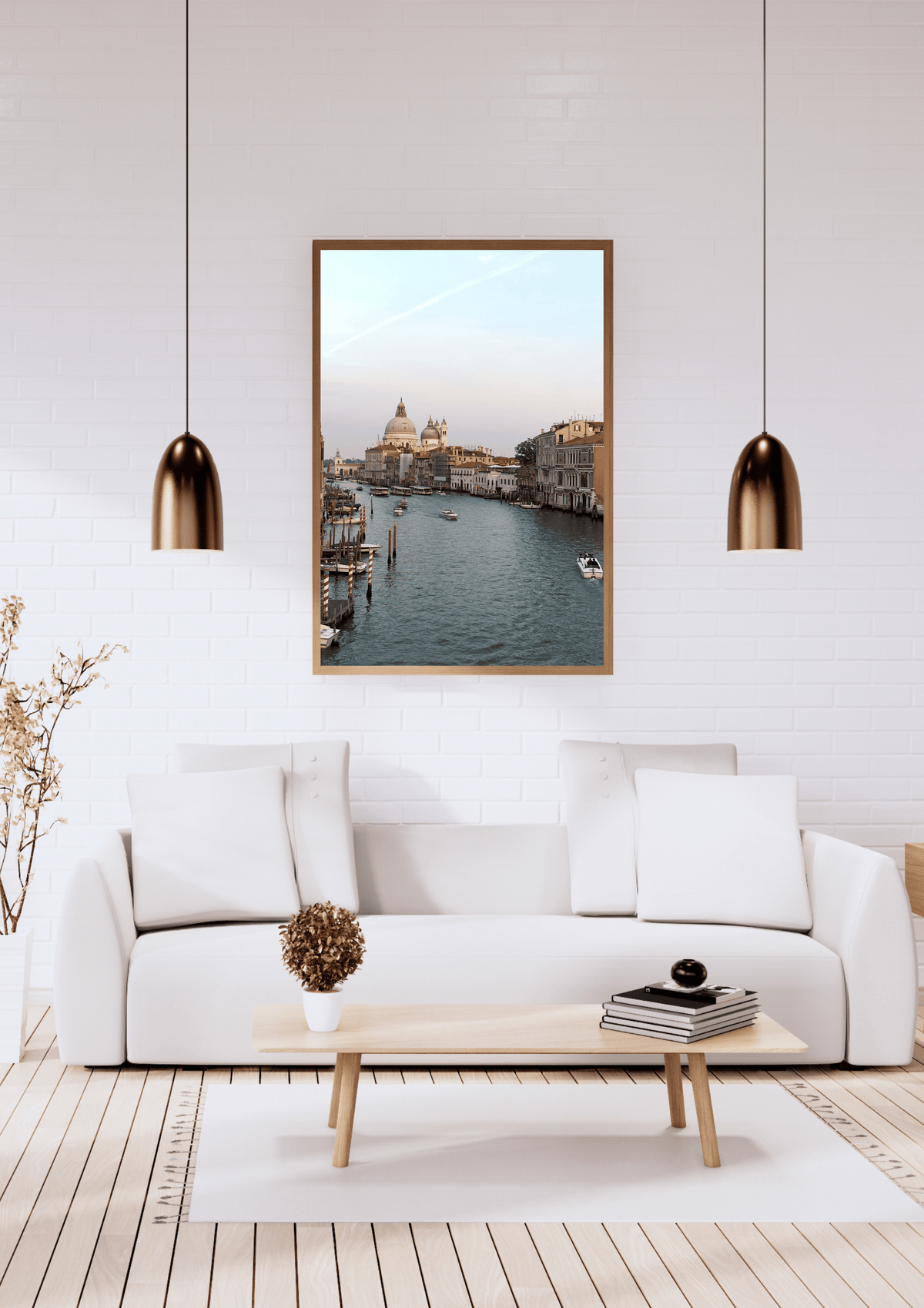 A framed art print depicting a scenic canal view of Venice, hung on a white brick wall above a modern white sofa in a bright, contemporary living room.