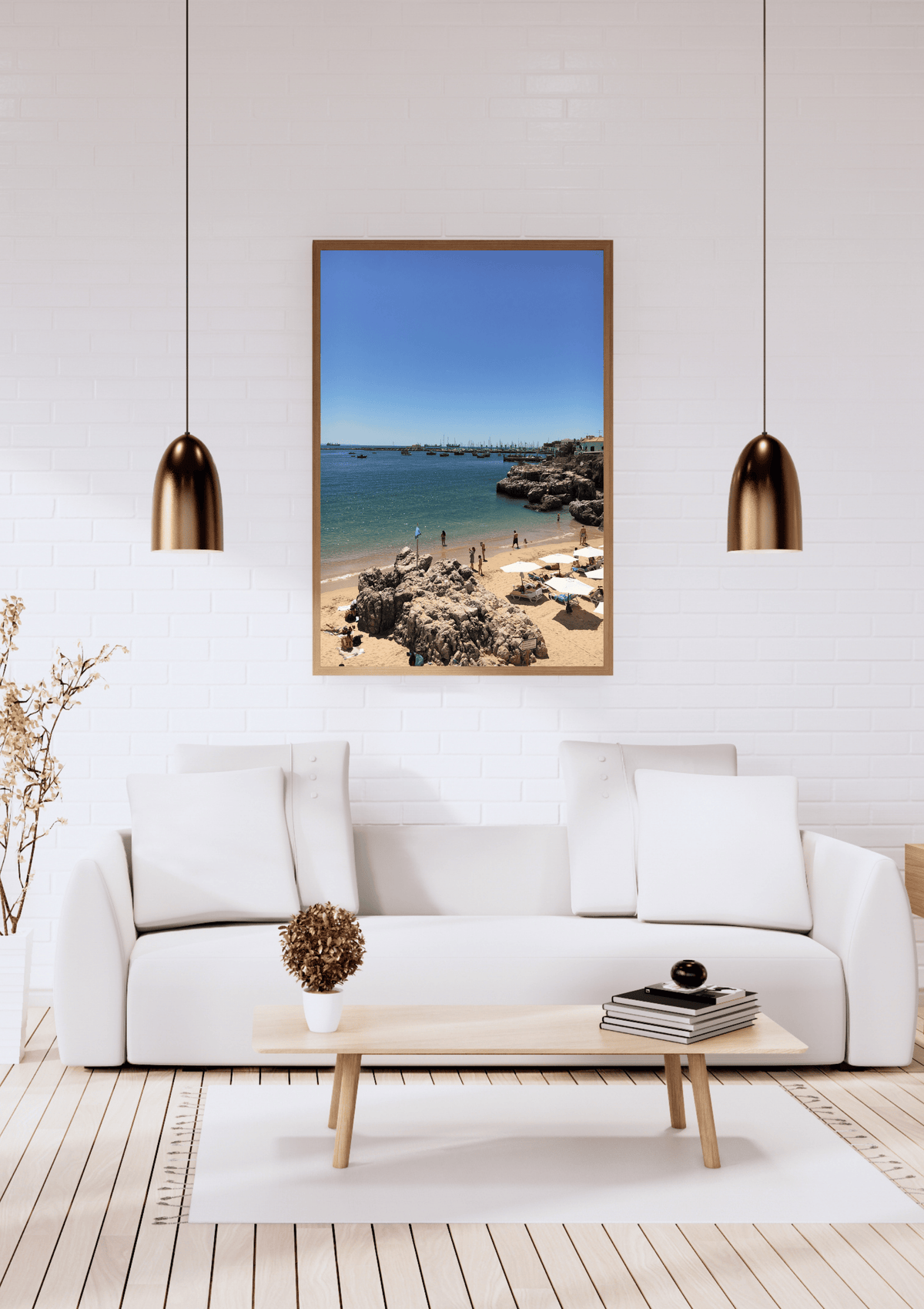 A framed vertical beach print with a blue sky, turquoise water, and sandy shore, displayed on a white brick wall above a modern white sofa in a bright living room.