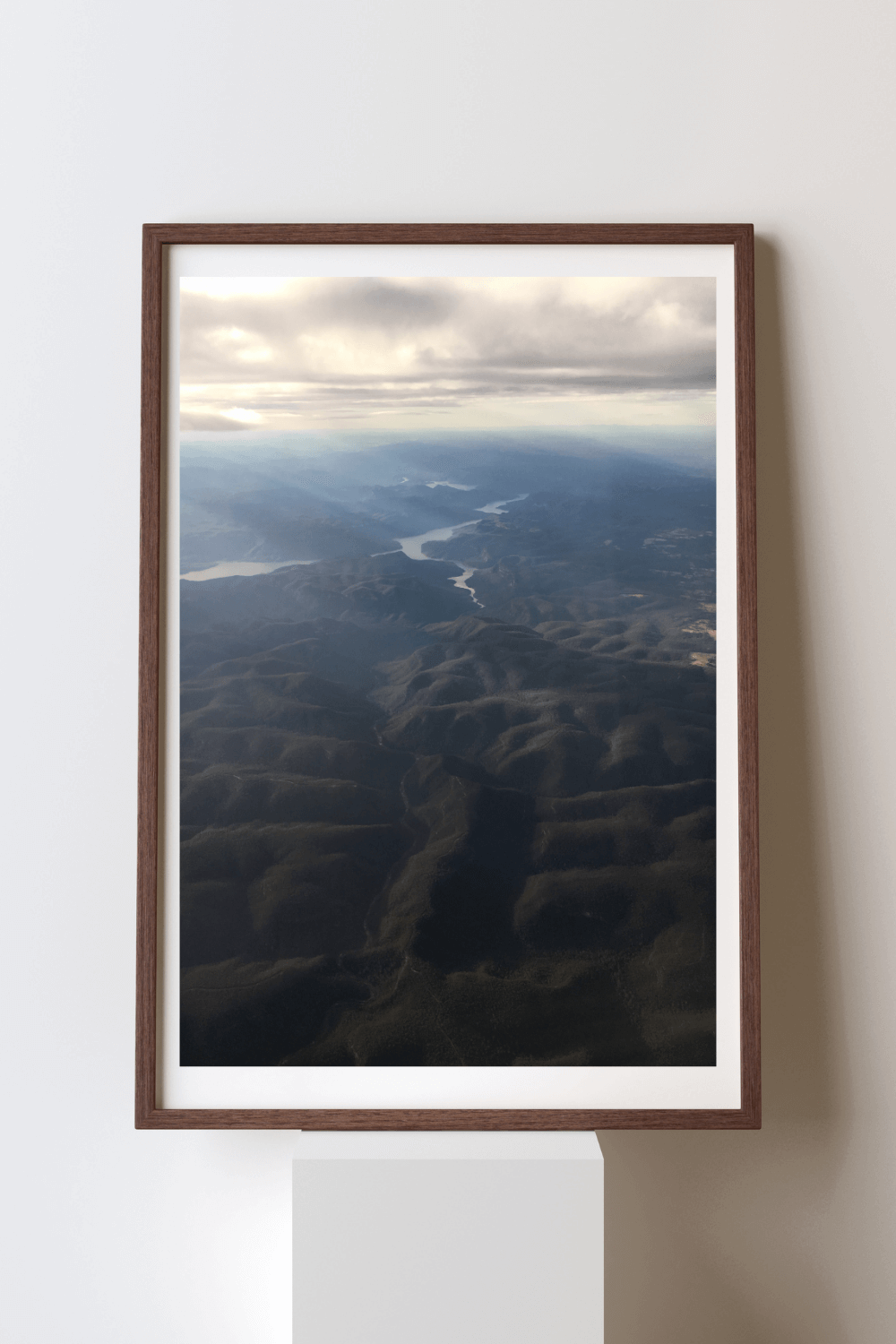 Heavens Above fine art travel photography print featuring an aerial view of the rays of light shining through clouds onto the dark blue and black mountains below in Australia