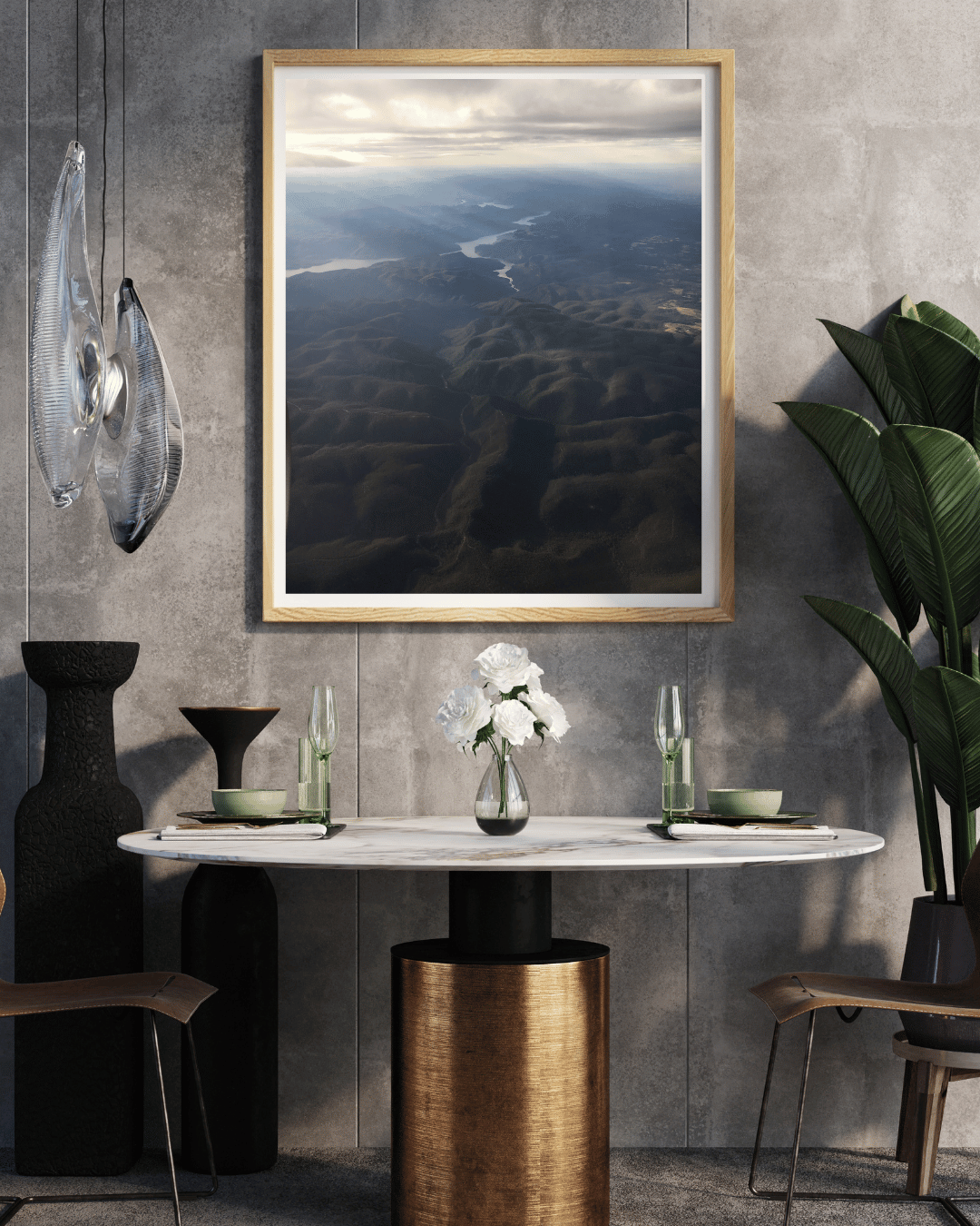 A framed landscape art print depicting an aerial view of the rays of light shining through clouds onto the dark blue and black mountains below, styled in a modern dining room setting above a marble-top table.