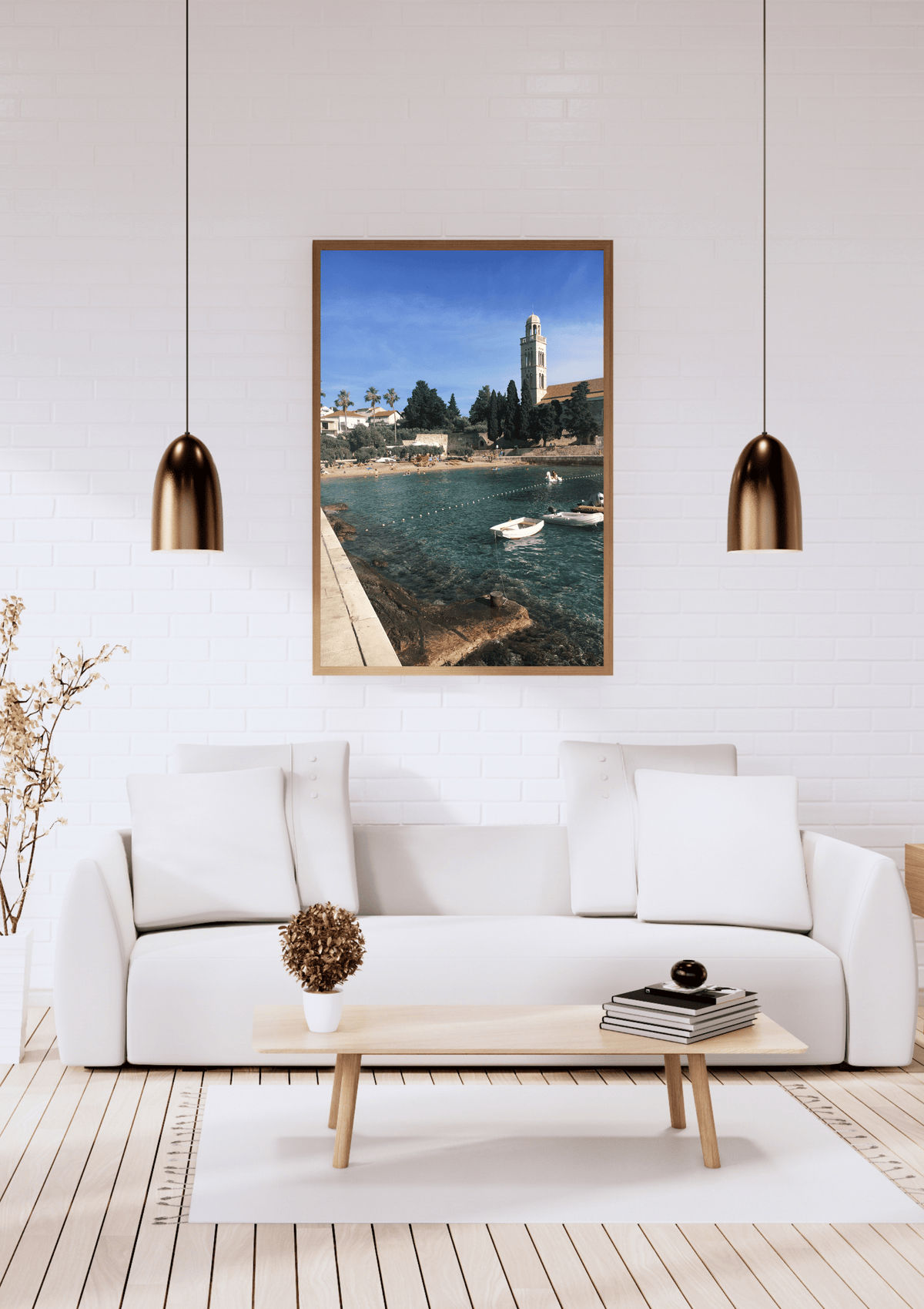 A framed art print depicting a scenic Croatian harbor with a tower and boats under a blue sky, displayed on a white brick wall above a modern white sofa in a bright living room.
