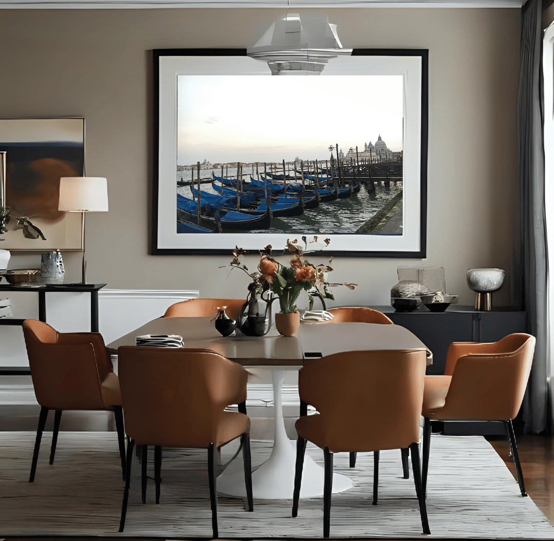 A large framed art print depicting blue gondolas in Venice hangs on a beige wall in a modern dining room setting with a dark wood table and six brown leather chairs.