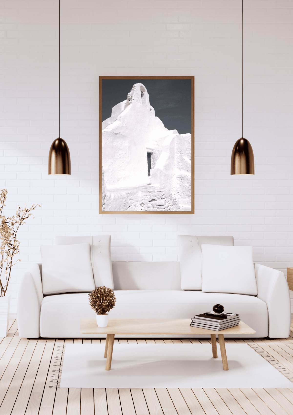 A framed black and white art print featuring a whitewashed building in Mykonos, Greece displayed on a white brick wall above a modern white sofa in a bright, contemporary living room.