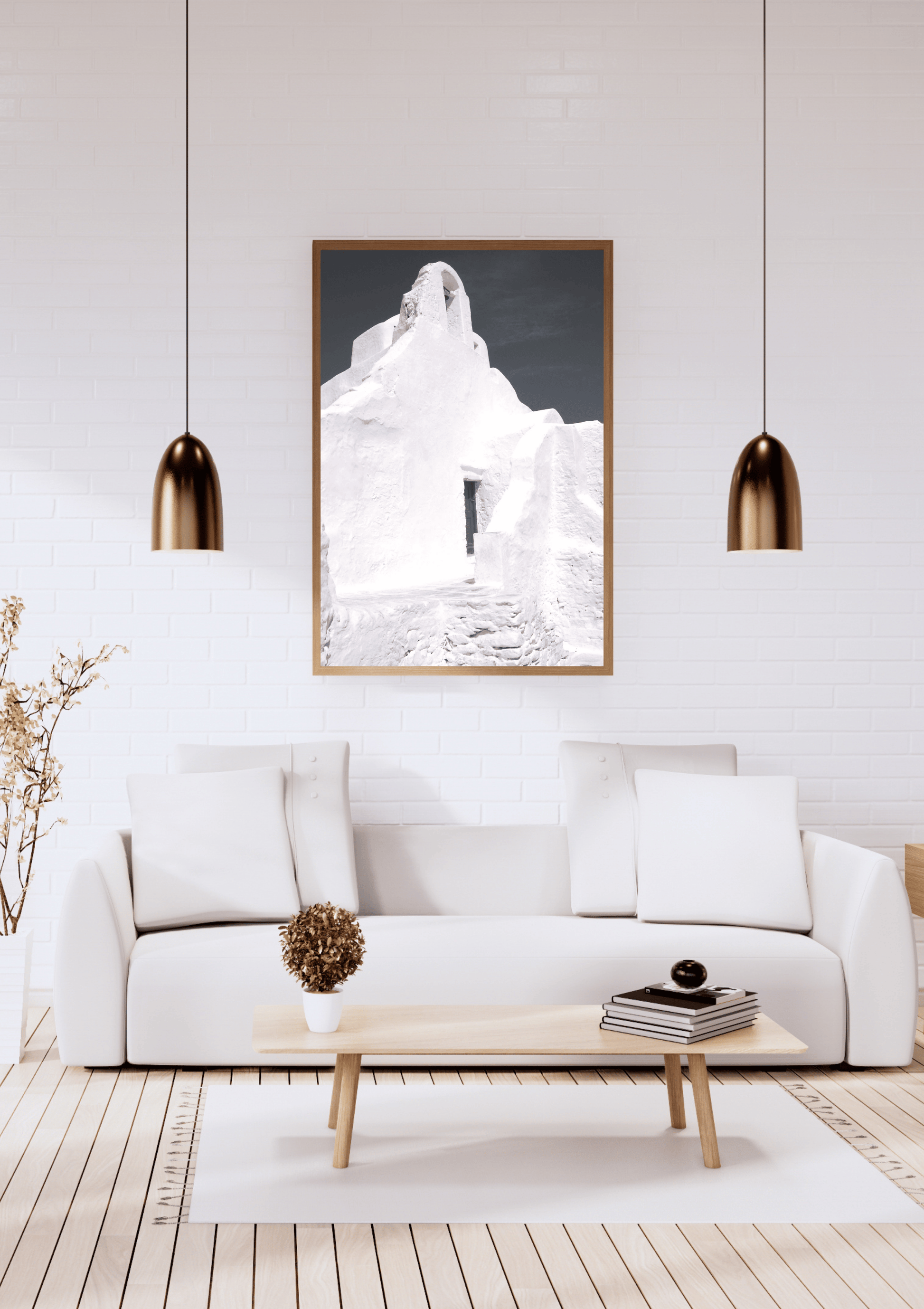 A framed black and white art print featuring a whitewashed building in Mykonos, Greece displayed on a white brick wall above a modern white sofa in a bright, contemporary living room.