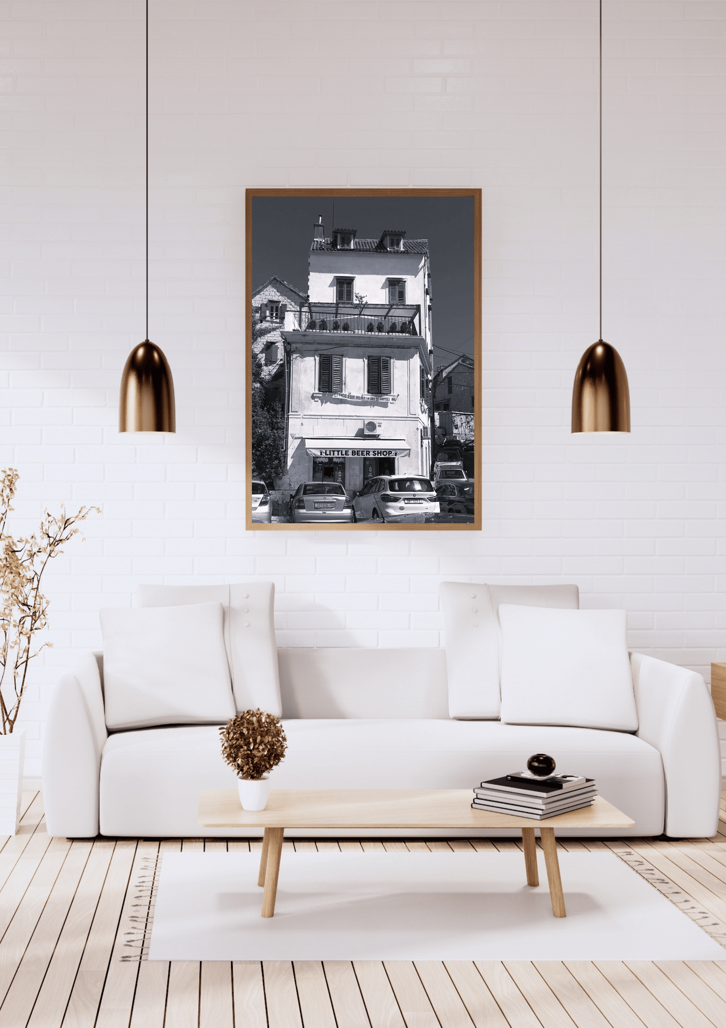 A framed black and white architectural photograph of a building, displayed on a white brick wall above a modern white sofa in a styled living room setting.