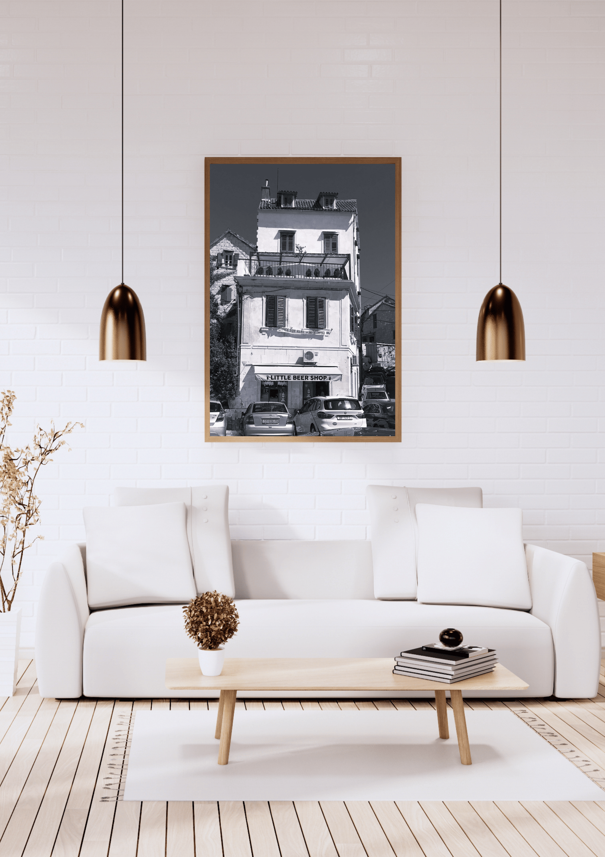 A framed black and white architectural photograph of a building, displayed on a white brick wall above a modern white sofa in a styled living room setting.