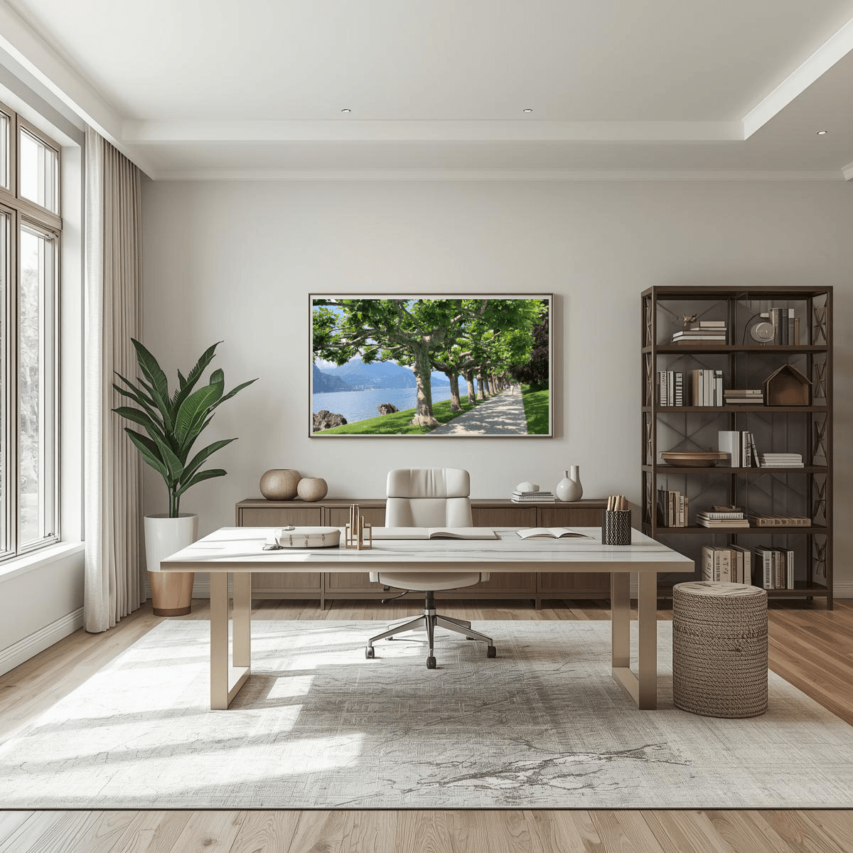 A large framed landscape art print depicting a scenic tree-lined path along  Lake Como, displayed on a neutral wall in a modern, sunlit home office with a desk, chair, and bookshelves.