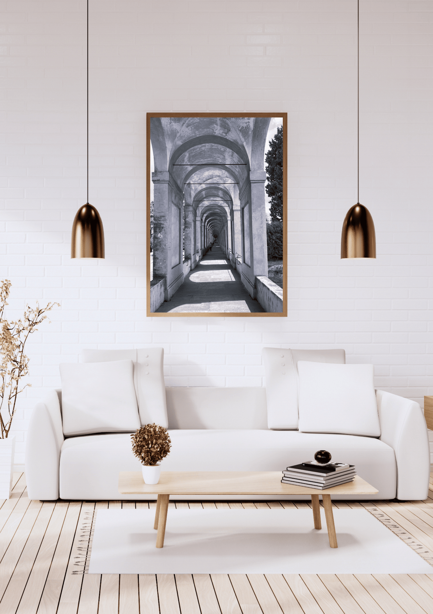 A framed black and white art print depicting an arched corridor, displayed on a white brick wall above a modern white sofa in a styled living room.