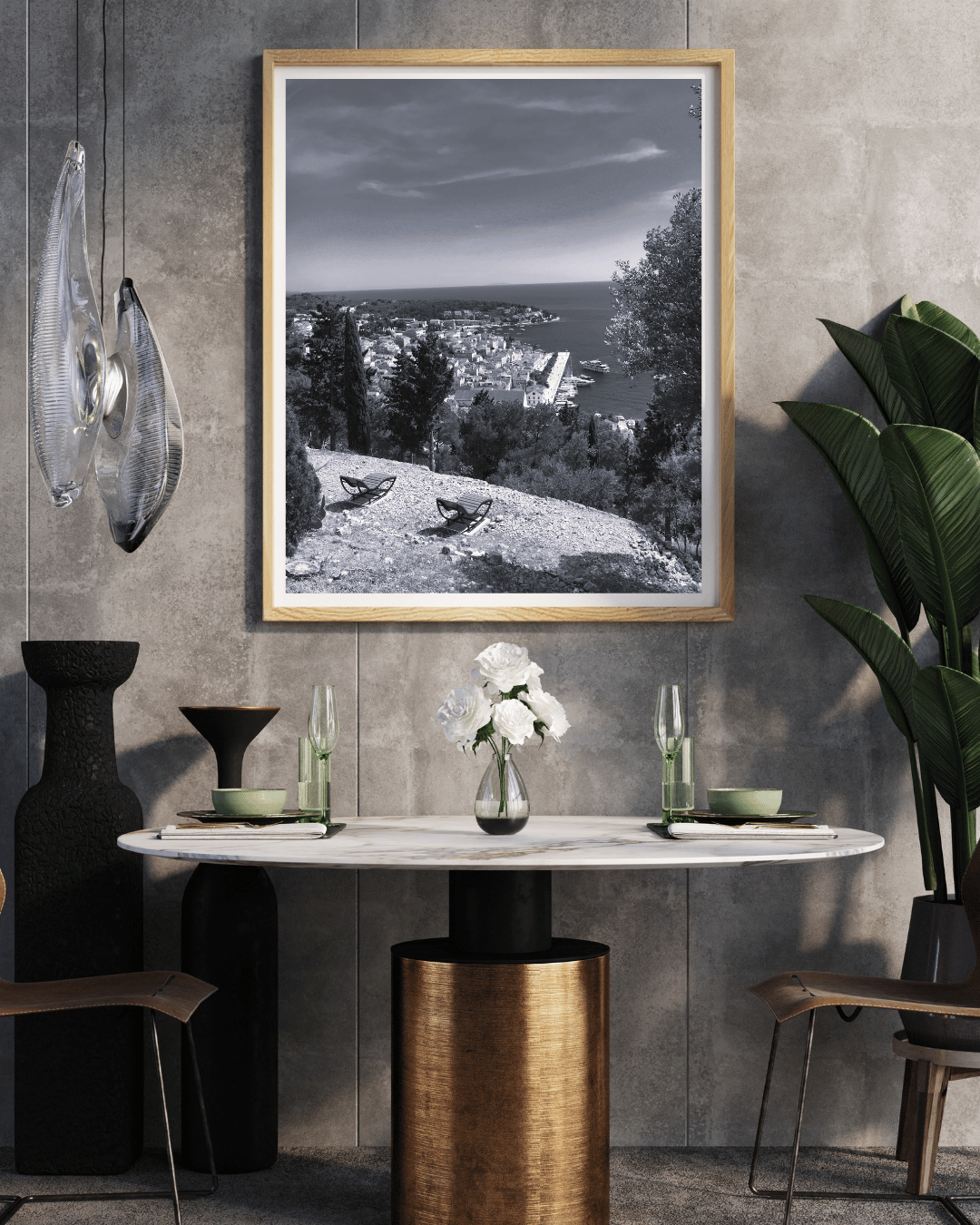 A framed black and white landscape photograph of a coastal town hanging on a textured gray wall above a dining table in a modern interior setting.