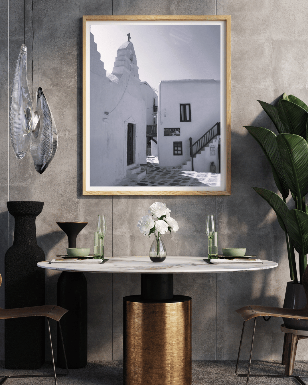 A framed black and white photograph of a Mediterranean village street with white buildings, displayed on a textured gray wall above a dining table in a modern styled room.